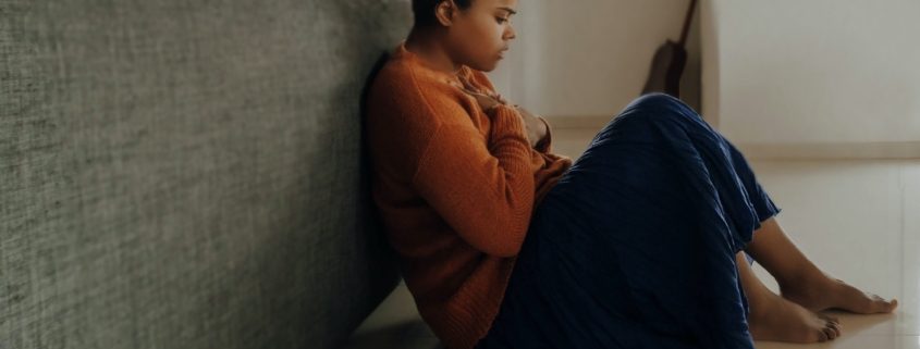 A girl is sitting on the floor against her bed.